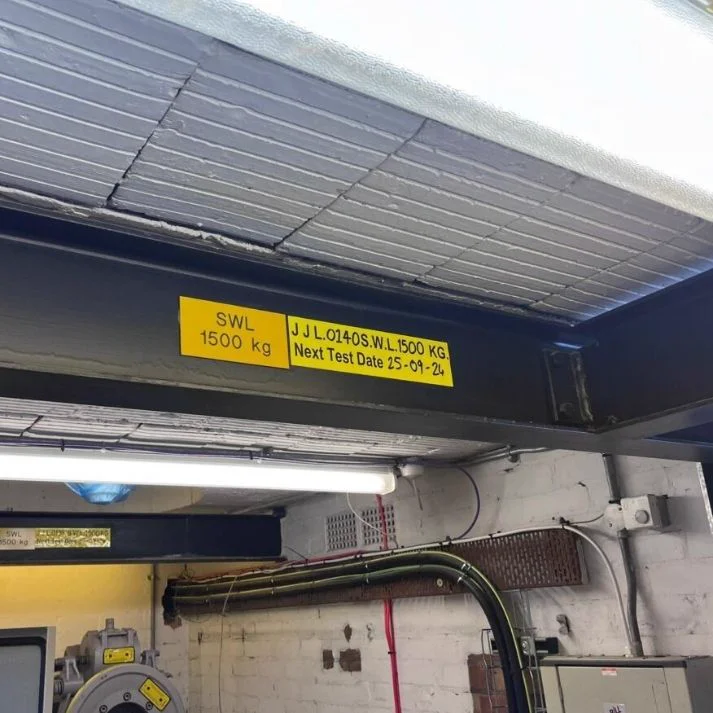 Installed lifting beam with yellow SWL 1500 kg plates and test date markings