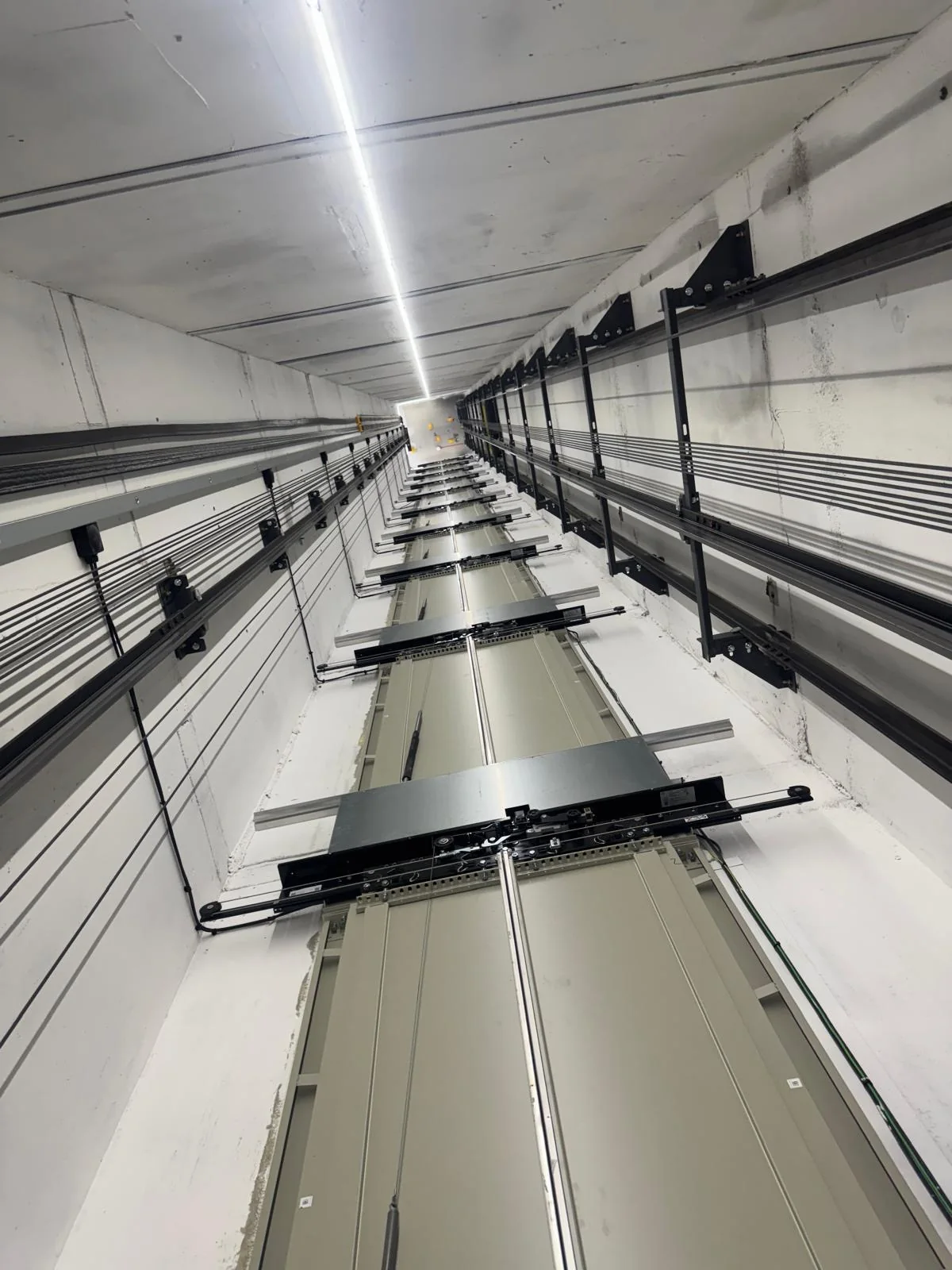 Looking along a lift shaft painted bright white, with an LED light strip and guide rails running its full length
