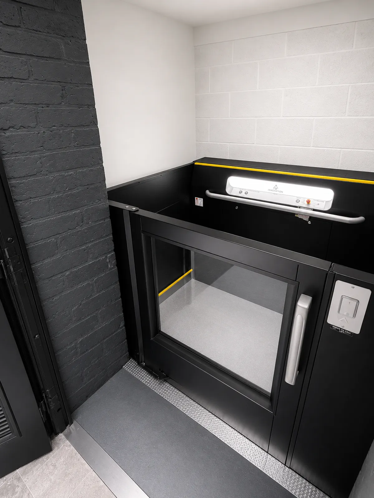 Black Aritco goods lift with half-height landing door and yellow safety edges