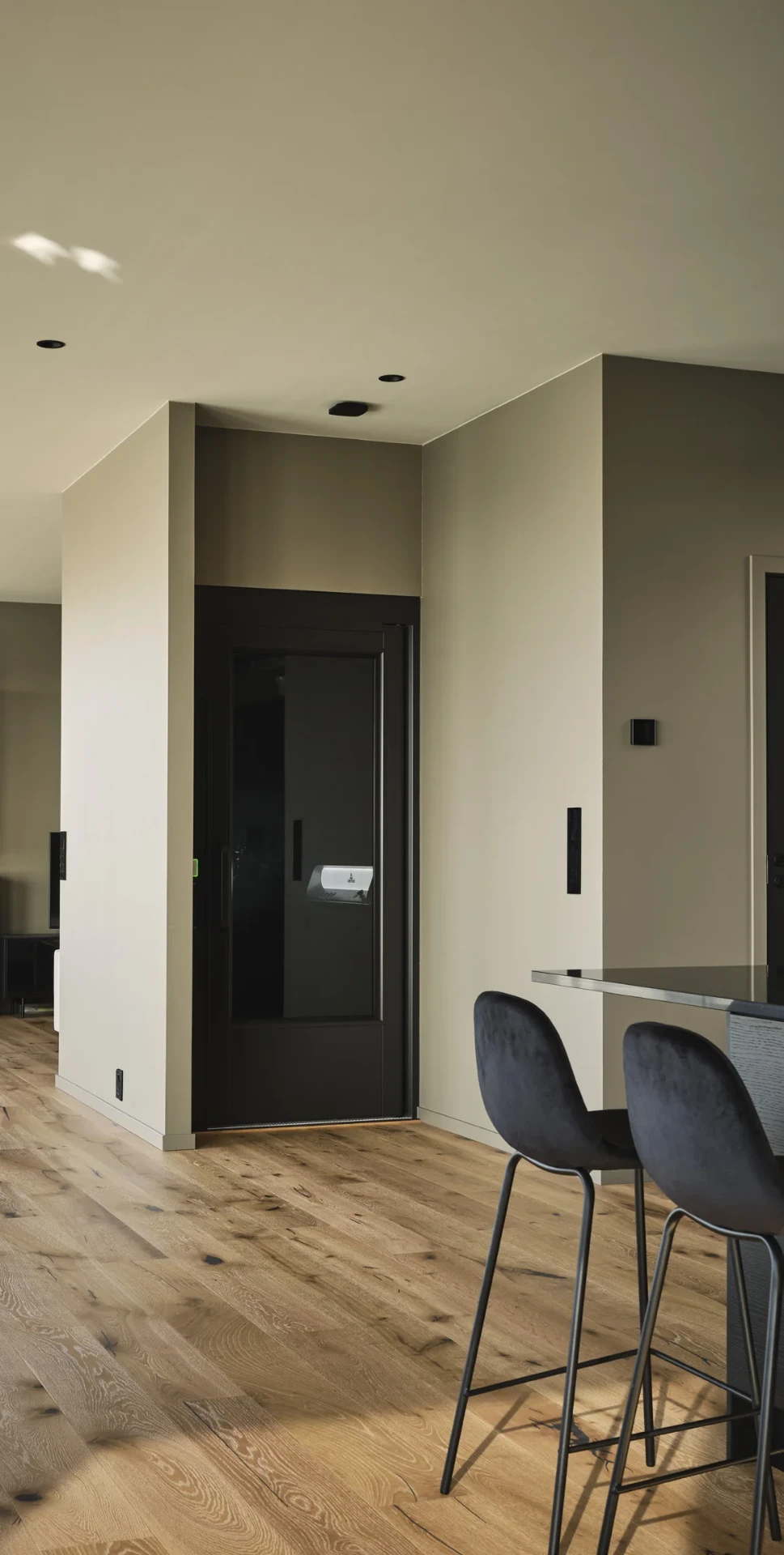 An Aritco HomeLift Access built flush into the wall of an open plan living space, its black landing door showing the control panel inside