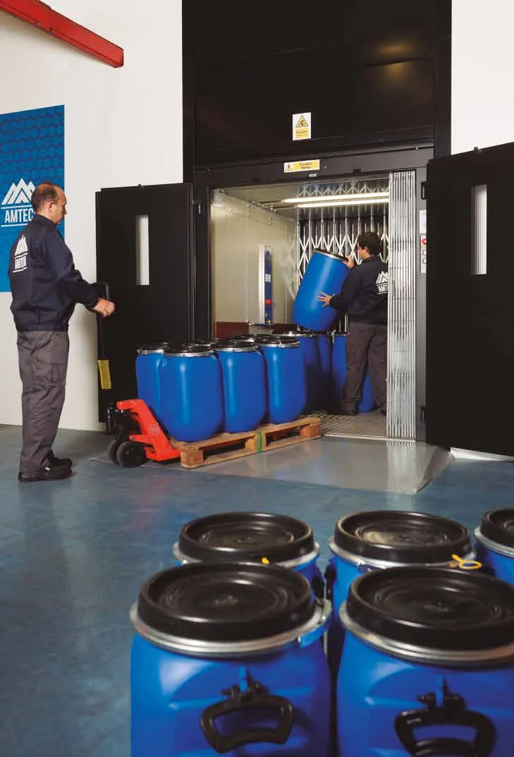 Blue drums on a pallet being wheeled into a goods lift, with more drums waiting in the foreground