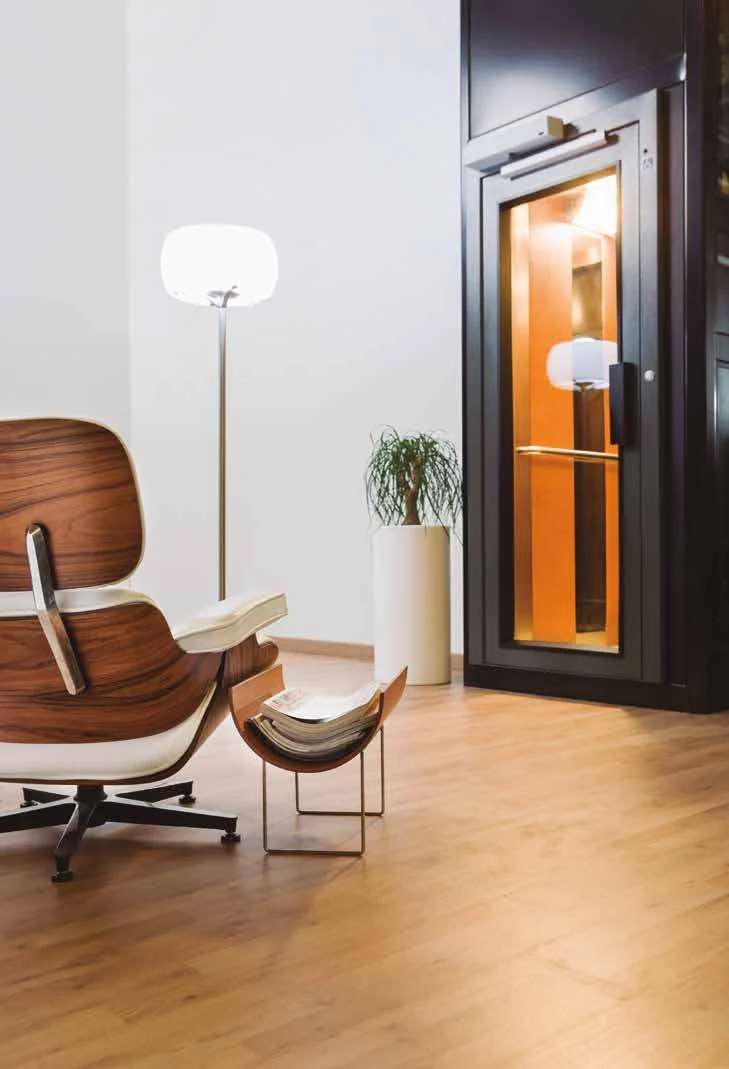 An Improlift with a glazed hinged door and a warm-lit cabin, beside a lounge chair and a floor lamp