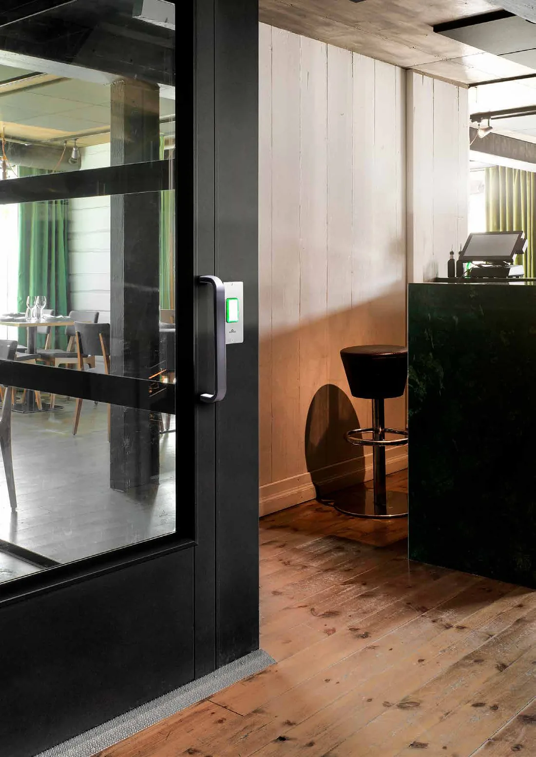 A black Aritco PublicLift Access with a glazed door, installed beside the bar of a restaurant with a timber floor